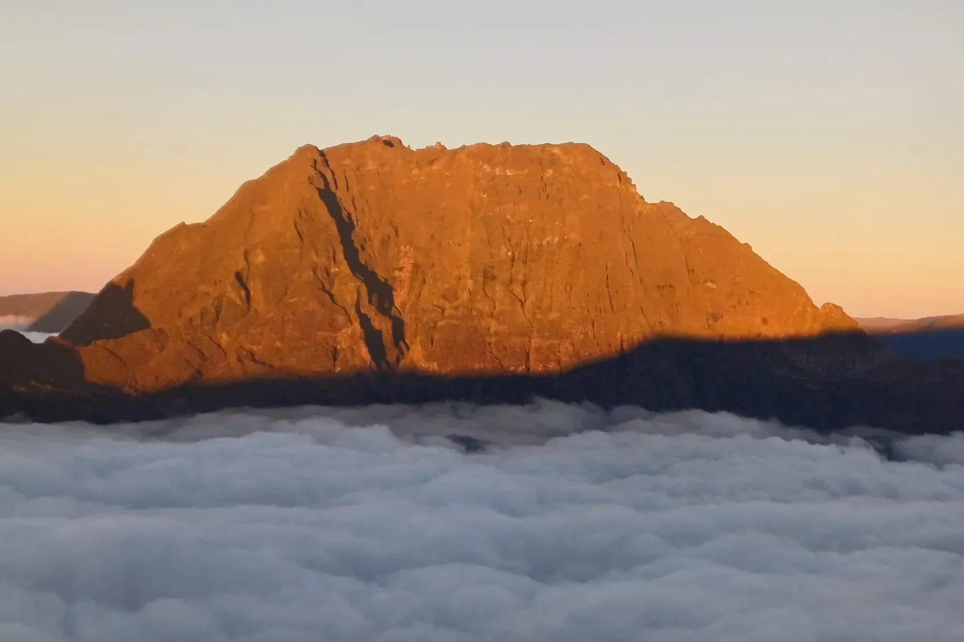 Un sommet embrasé par le soleil levant, au-dessus d’une mer de nuages.