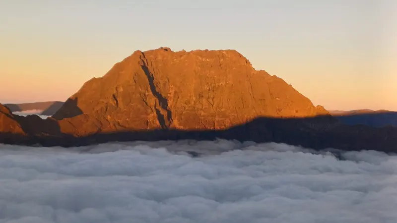 Un sommet embrasé par le soleil levant, au-dessus des nuages